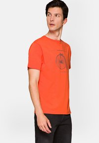 Jasnopomarańczowa koszulka wykonana z bawełny, z ciemnym grafiką roweru na środku. Krótkie rękawy i klasyczny krój z okrągłym dekoltem.