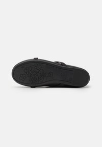 Suela de sandalia negra con una superficie de goma texturizada. Presenta un grabado de patrón floral y una zona de talón flexible para mayor comodidad.