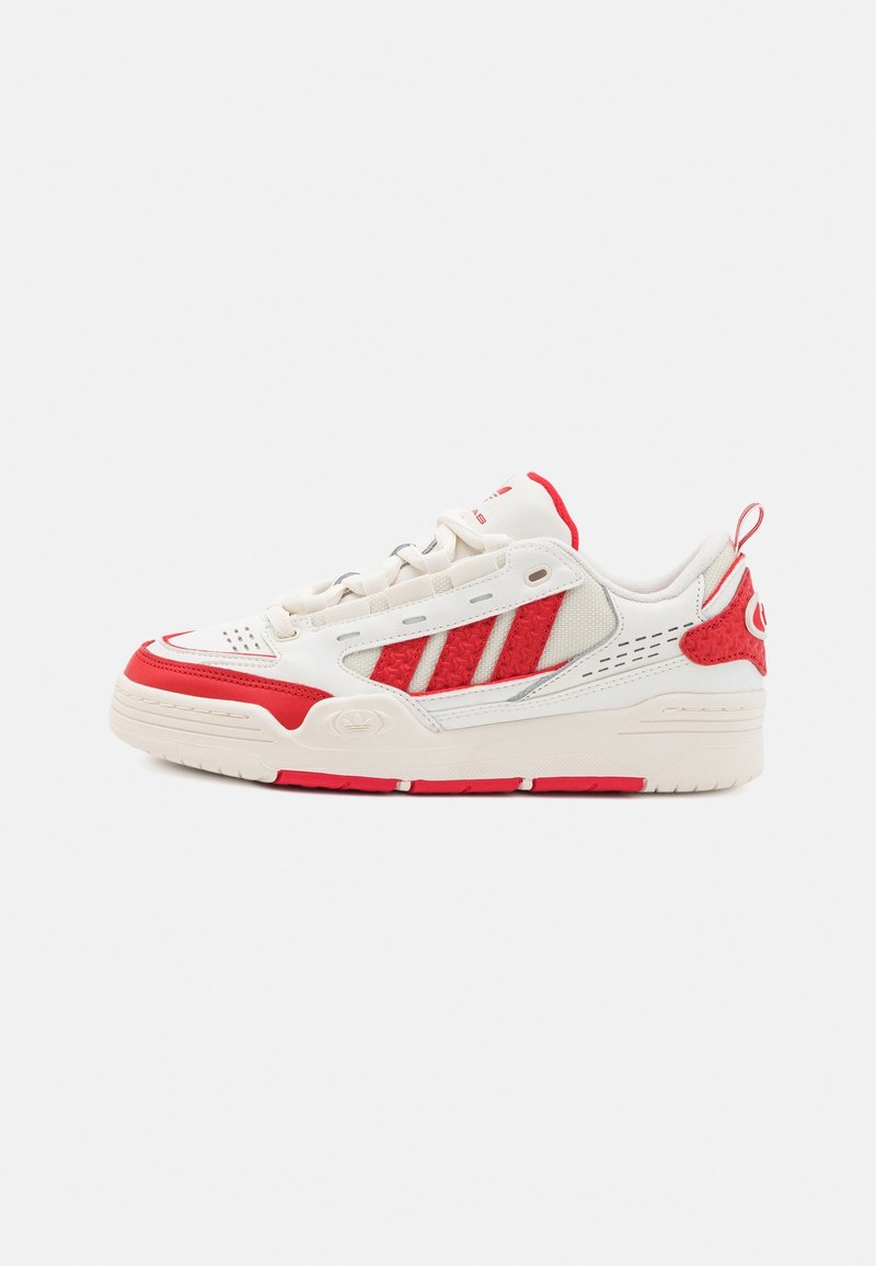 White sneakers with red accents, mesh and synthetic materials, featuring three horizontal stripes, a textured side panel, and a pull tab.