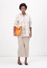 Καρό μπεζ πουκάμισο με κουμπιά, γκρι φούστα cargo και μαύρες μπαλαρίνες. Κρατά μια πορτοκαλιά δερμάτινη τσάντα με ξεχωριστή λαβή σε σχήμα κοπής.
