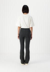 Pantaloni neri a campana con un alto punto vita, realizzati in un tessuto elasticizzato. Abbinati a una maglietta bianca a maniche larghe, visti da dietro.