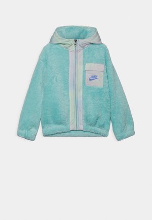Veste à capuche en peluche bleu clair avec fermeture éclair à l'avant et petite poche, arborant le logo Nike bleu sur la poitrine.
