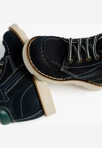 Chaussures en daim noir avec coutures blanches, bouts ronds et semelles en caoutchouc beige. Caractéristiques : œillets en métal et fermeture éclair sur le côté.