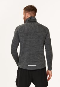 Grå tekstureret pullover med høj krave. Har en reflekterende stribe på bagsiden og lange ærmer, designet til atletisk brug.