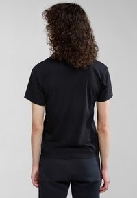 Černé bavlněné tričko viděné zezadu. Krátké rukávy, kulatý výstřih, minimalistický design, hladká textura a uvolněný střih.