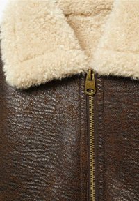 Veste en cuir marron texturé avec une fermeture éclair dorée et un col en sherpa crème et doux.