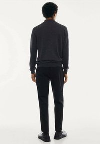 Dunkelgrauer gestrickter Pullover mit Kragen, kombiniert mit schwarzen Slim-Fit-Hosen. Das Outfit zeichnet sich durch eine glatte Textur und ein minimales Design aus.