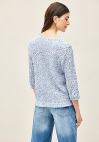 Haut en tricot bleu clair avec un motif texturé, manches trois-quarts et col rond. Porté avec un jean large bleu clair.