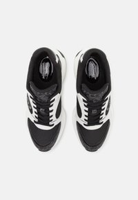 Baskets athlétiques noires et blanches avec une tige en mesh, des accents texturés et une semelle arrondie, avec des lacets et un logo en détail sur la languette.