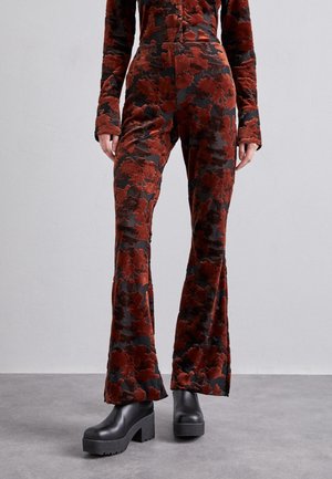 Slim fit, flared pants with red and dark floral pattern, worn with matching long-sleeve top and black platform ankle boots on gray floor.