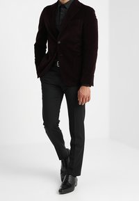 Blazer in cotone a coste color bordeaux con rever a punta, abbinato a pantaloni neri aderenti e scarpe nere lucide, creando un look formale su misura.