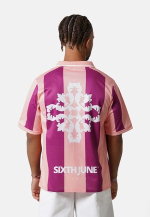 Man met gevlochten haar die een paars-roze gestreept shirt met korte mouwen draagt met een wit sierlijk ontwerp en tekst op de achterkant.