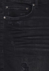 Tissu en denim noir avec une texture délavée, des zones usées et une petite poche avant. Des accessoires en métal argenté complètent le design.