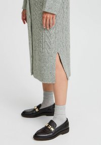 Vestido de punto gris con patrón de cable y abertura lateral, combinado con mocasines negros texturizados con herrajes dorados y calcetines gris de tobillo.