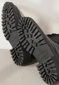 Calzature nere con una suola in gomma testurizzata caratterizzata da scanalature profonde e un motivo di battistrada, progettate per offrire trazione e durabilità.