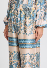 Helle Stoffhosen mit einem Paisley- und Blumenmuster in Blau und Gold. Merkmale umfassen einen elastischen Bund und gemusterte Akzente.