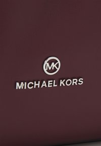 Bordowa skórzana torebka z logo Michael Kors w srebrnym kolorze i teksturowaną powierzchnią. Prosty design z okrągłym akcentem i nazwą marki.