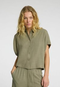 Short-sleeve olive green button-up shirt made of lightweight fabric, featuring a relaxed fit and a subtle texture. Smooth surface with a collar.