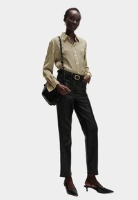 Blusa a maniche lunghe a righe gialla e nera, abbinata a pantaloni in finta pelle nera attillati. Gli accessori includono una piccola borsa nera e scarpe con tacco.