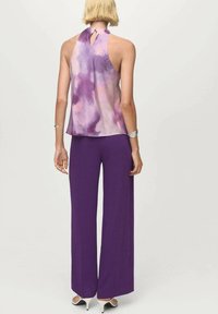 Pantalons larges violets associés à un haut sans manches à col halter en dégradé de violet et rose, avec un détail en clé à l'arrière.