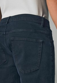 Donkerblauwe spijkerbroek met een gladde textuur, met een klassieke vijfzakkenstijl en subtiele witte stiksels langs de naden.