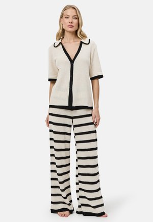 Mujer con parte superior de punto de manga corta color crema con botones y ribete negro, y pantalones anchos de punto a juego con rayas horizontales negras.