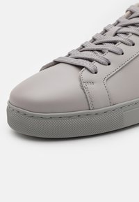 Γκρι δερμάτινα αθλητικά παπούτσια με στρογγυλή μύτη, υφή στη γκρι καουτσούκ σόλα και επίπεδα κορδόνια. Καθαρός σχεδιασμός με ελάχιστες ραφές.