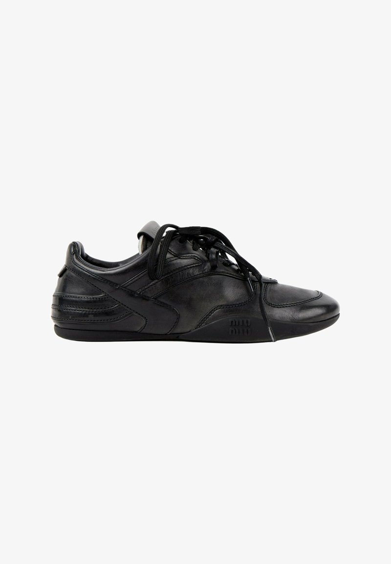 Basket en cuir noir avec lacets, semelle basse et design de panneaux cousus, vue de côté sur fond blanc.