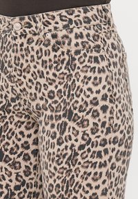 Džíny s leopardím potiskem, které mají béžové pozadí s černými a hnědými skvrnami. Vyrobeno z denimu s klasickým designem pěti kapes.