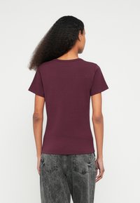 Μπορντό κοντομάνικη μπλούζα με στρογγυλή λαιμόκοψη, εφαρμοστή γραμμή και λεία υφή. Συνδυάζεται με γκρι τζιν με ελαφρώς φθαρμένη όψη, παρουσιάζοντας απλή πίσω όψη.