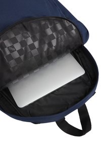 Marinblå ryggsäckens inre med ett vadderat fack för en bärbar dator, med ett svart rutigt foder och robust dragkedja. Svart tygdetaljer.