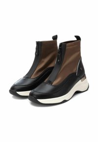 Botas de tobillo negras y marrones con un acabado suave y texturizado, que cuentan con una cremallera frontal y una suela blanca para contraste.