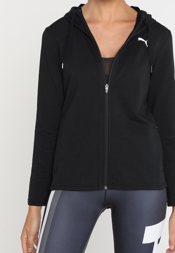 Femme portant un sweat à capuche noir zippé avec le logo Puma et des leggings gris foncé avec une bande blanche et un motif de chiffres.