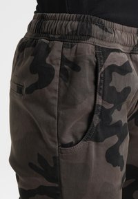 Kamouflagemönster joggerbyxor i mörkgrå och svart, med elastisk midja och sidficka, i ett slätt, texturerat tyg.