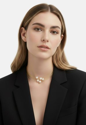 Gouden draadchoker met drie clusters witte parels, gedragen over een zwarte blazer; gladde textuur met glanzende parelaccenten.