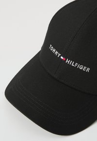 Black baseball cap with a structured shape. Features white embroidered text "TOMMY HILFIGER" and a small red, white, and blue logo detail.