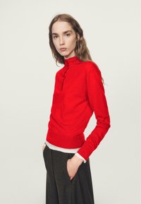 Top rosso a maniche lunghe con collo alto e patta con tre bottoni, con una silhouette aderente e dettaglio a contrasto di orlo bianco.