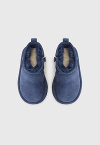 Mules en suède bleu avec une doublure en fausse fourrure douce, dotés de deux zips sur les côtés et de bords arrondis pour un ajustement confortable.
