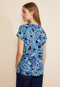 Camicia a maniche corte con stampa paisley blu e verde, caratterizzata da una vestibilità rilassata e un tessuto morbido con una leggera lucentezza e un dettaglio a piega sul retro.