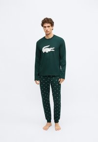 Top de pijama verde de manga larga con un gráfico de cocodrilo blanco, combinado con pantalones a juego que presentan pequeños patrones de cocodrilos blancos. Tela suave.