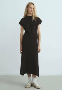 Conjunto negro de dos piezas que incluye una blusa ajustada de manga corta y una falda de longitud media. Combinado con zapatillas beiges y calcetines blancos.