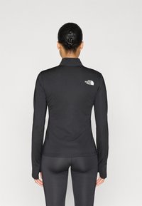 Μαύρο αθλητικό τοπ με μακριά μανίκια, ψηλό γιακά και διακριτικό λογότυπο στο επάνω μέρος της πλάτης. Ομαλή υφή και εφαρμοστή σχεδίαση για αθλητική χρήση.