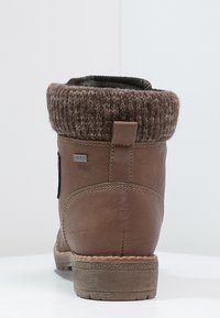 Hnědá kožená kotníková bota s pleteným textilním lemem, texturovanou podrážkou a malou logo visačkou na boku, se zaobleným tvarem a robustní konstrukcí.