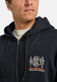 Marine blue zip-up hoodie met een trekkoordkap, voorzien van witte grafische ontwerpen en oranje tekst ''BILLABONG ADVENTURE DIVISION'' op de borst.