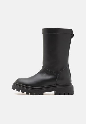 Schwarzer Lederstiefel mittlerer Wadenhöhe mit klobiger Profilsohle und Reißverschluss hinten, seitlich auf schlichtem hellem Hintergrund dargestellt.