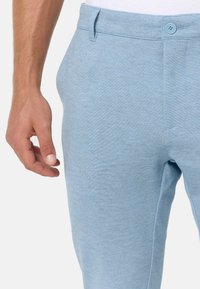 Světle modré volnočasové kalhoty vyrobené z měkké texturované látky; mají zapínání na knoflík a boční kapsy. Hladký, pohodlný střih.