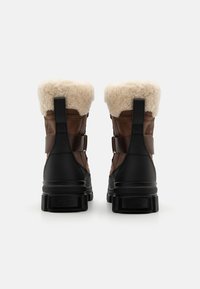Brune lærstøvler med sorte gummisåler og en hvid imiteret pelskrave. Har en sidestrag og mærket detalje på bagsiden. Holdbart design.