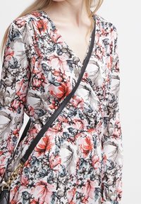 Abito floreale con scollo a V, caratterizzato da un motivo di fiori neri e rossi su uno sfondo bianco, maniche lunghe e una tracolla nera.