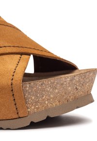 Tan suede sandal with crossover straps, cork wedge heel, textured brown footbed, and rubber outsole with traction details.