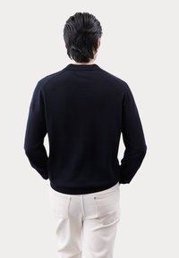 Marineblå strikket sweater med en tætsiddende design og ribbede kanter. Båret med lys beige bukser, der viser en glat tekstur og rene linjer.